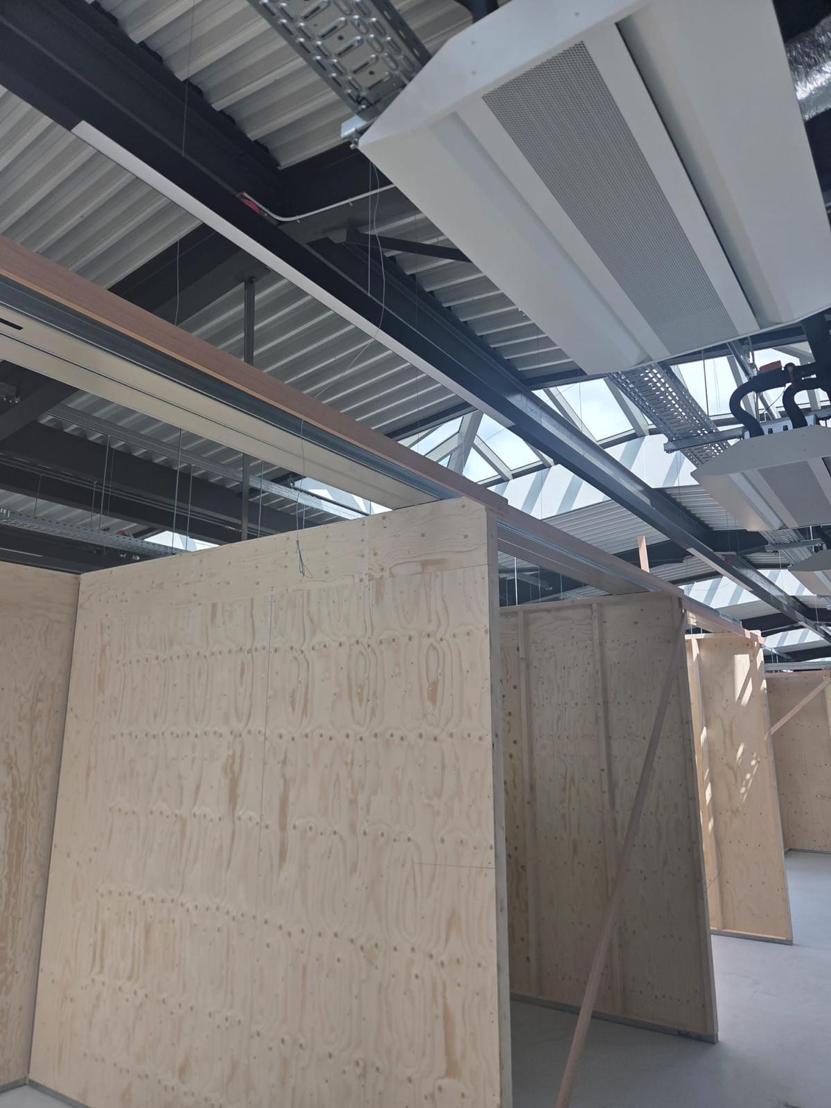 Vrijstaande houten cabines in een bedrijfshal onder daklichten en zichtbare installaties