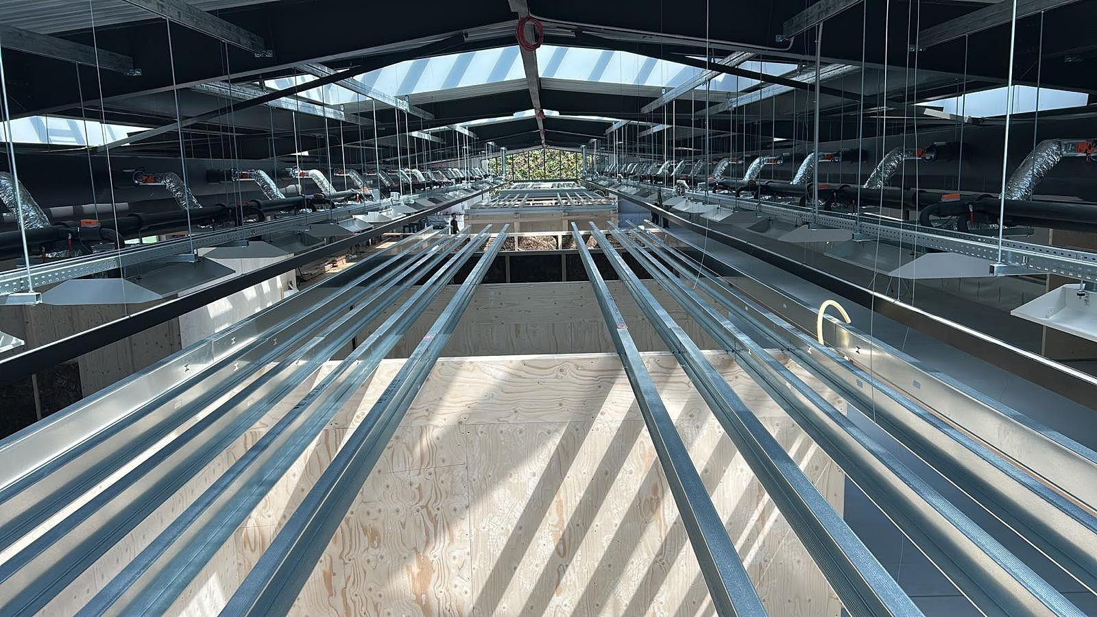 Lange rij verzinkte metalstud profielen in perspectief door een bedrijfshal met daklichten